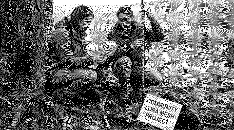 Dithered image: two people install a community LoRa mesh antenna in a forest.
